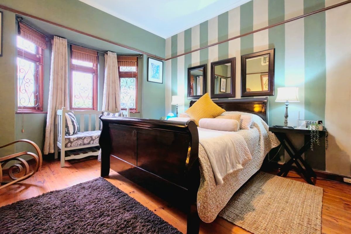 A well-maintained bedroom featuring classic timber flooring, a bay window with decorative leaded glass, and traditional picture rail detailing.