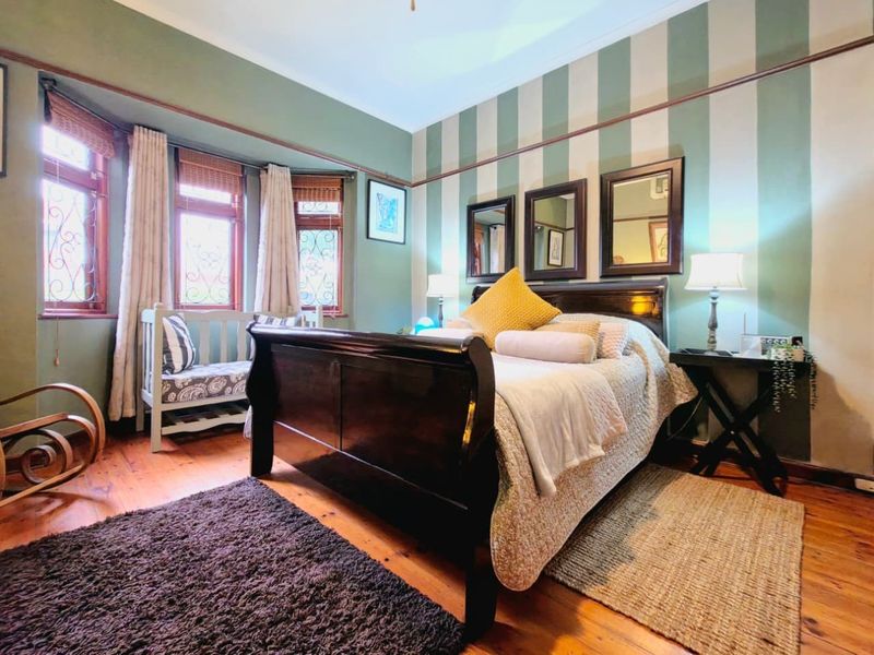 A well-maintained bedroom featuring classic timber flooring, a bay window with decorative leaded glass, and traditional picture rail detailing.