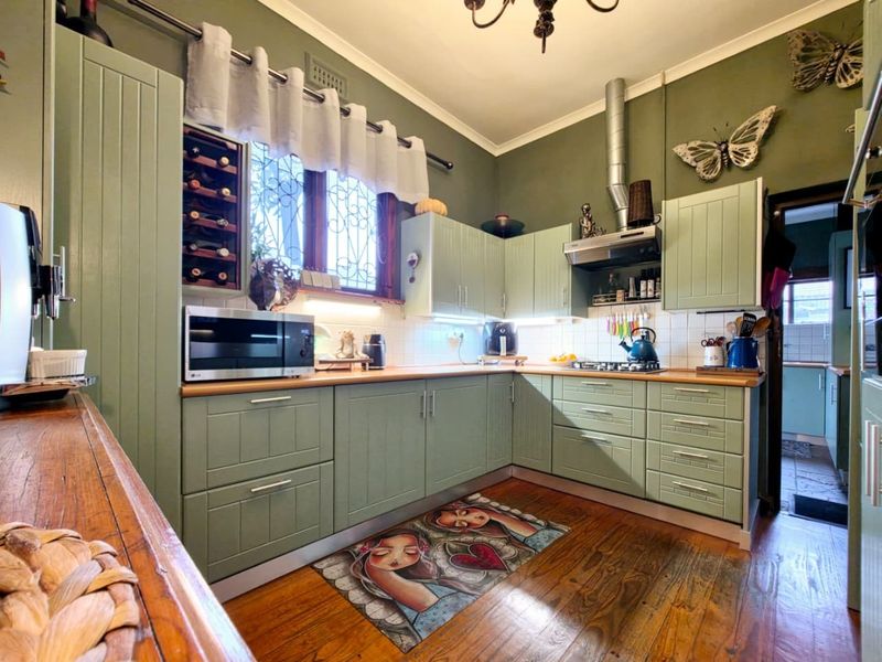 A well-maintained kitchen featuring sage green cabinetry, wooden countertops, a tiled backsplash, and hardwood flooring, offering a functional and characterful cooking space.