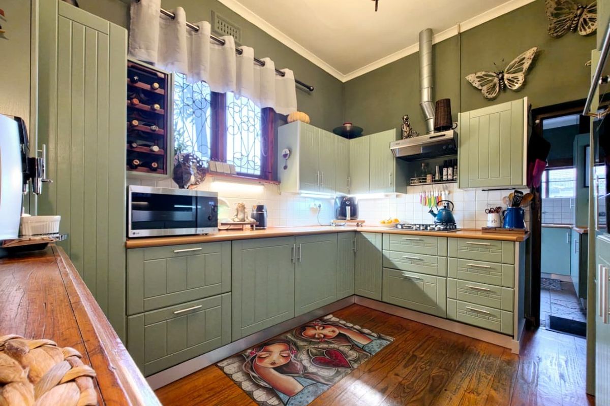 A well-maintained kitchen featuring sage green cabinetry, wooden countertops, a tiled backsplash, and hardwood flooring, offering a functional and characterful cooking space.