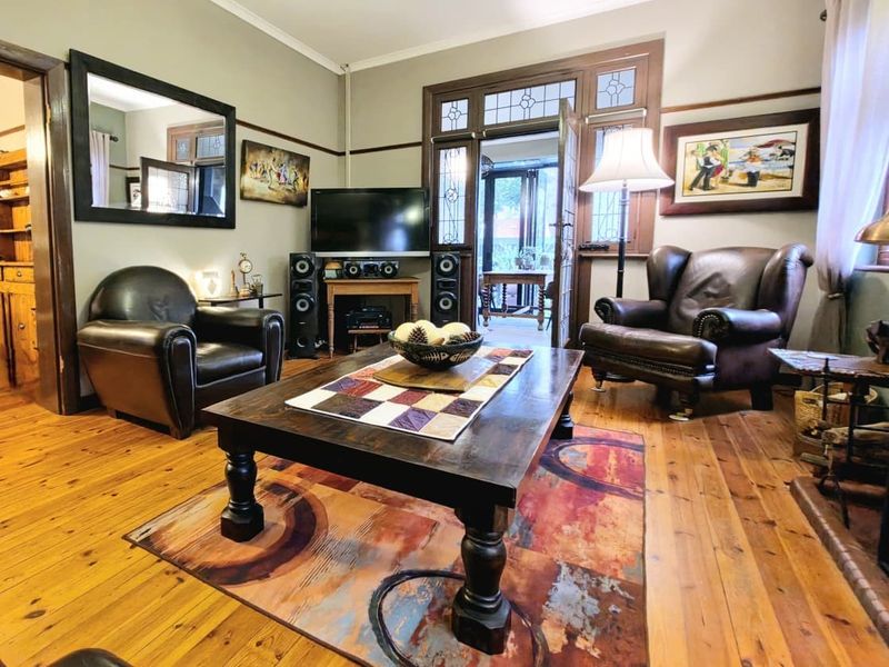 A cozy living room featuring warm hardwood timber flooring, classic picture rails, and a characterful leaded glass door leading to an adjoining space.