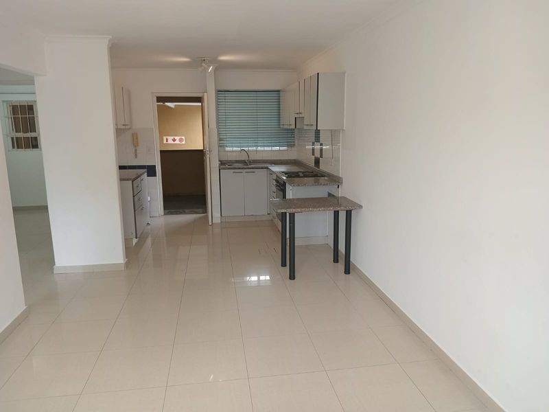 A clean, empty kitchen featuring white cabinetry, stone countertops, built-in appliances, and neutral tiled flooring, offering a functional and well-maintained space.
