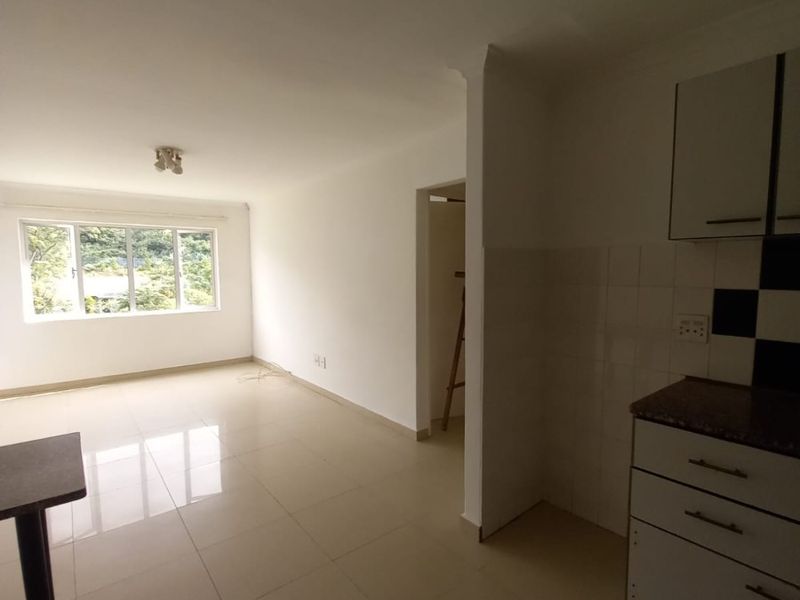 An open-plan living and kitchen area featuring neutral tiled flooring, white cabinetry, and granite countertops, offering a bright and versatile living space.