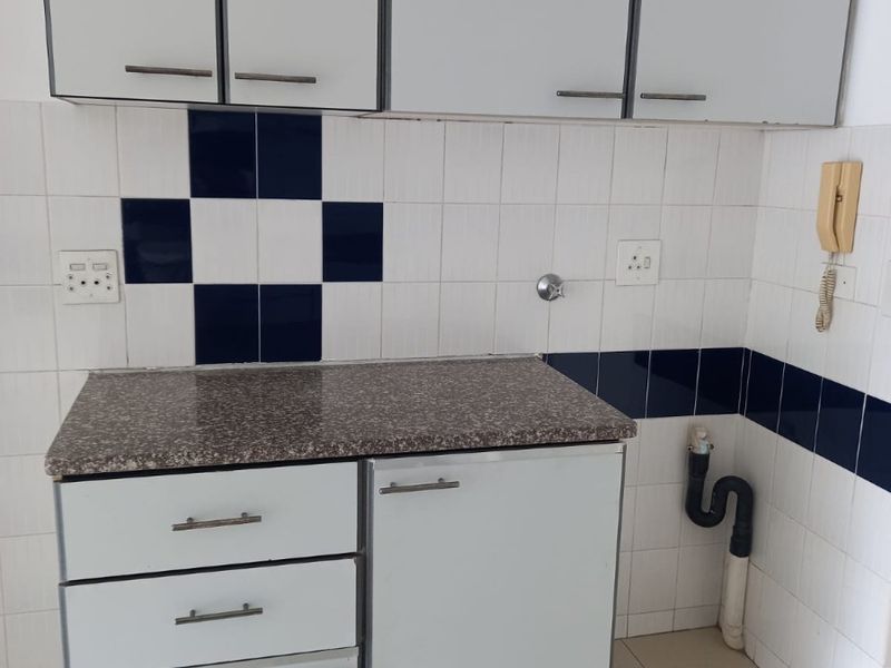 A compact kitchen area featuring white built-in cabinetry, a granite-look laminate countertop, and a tiled backsplash with an exposed plumbing connection.