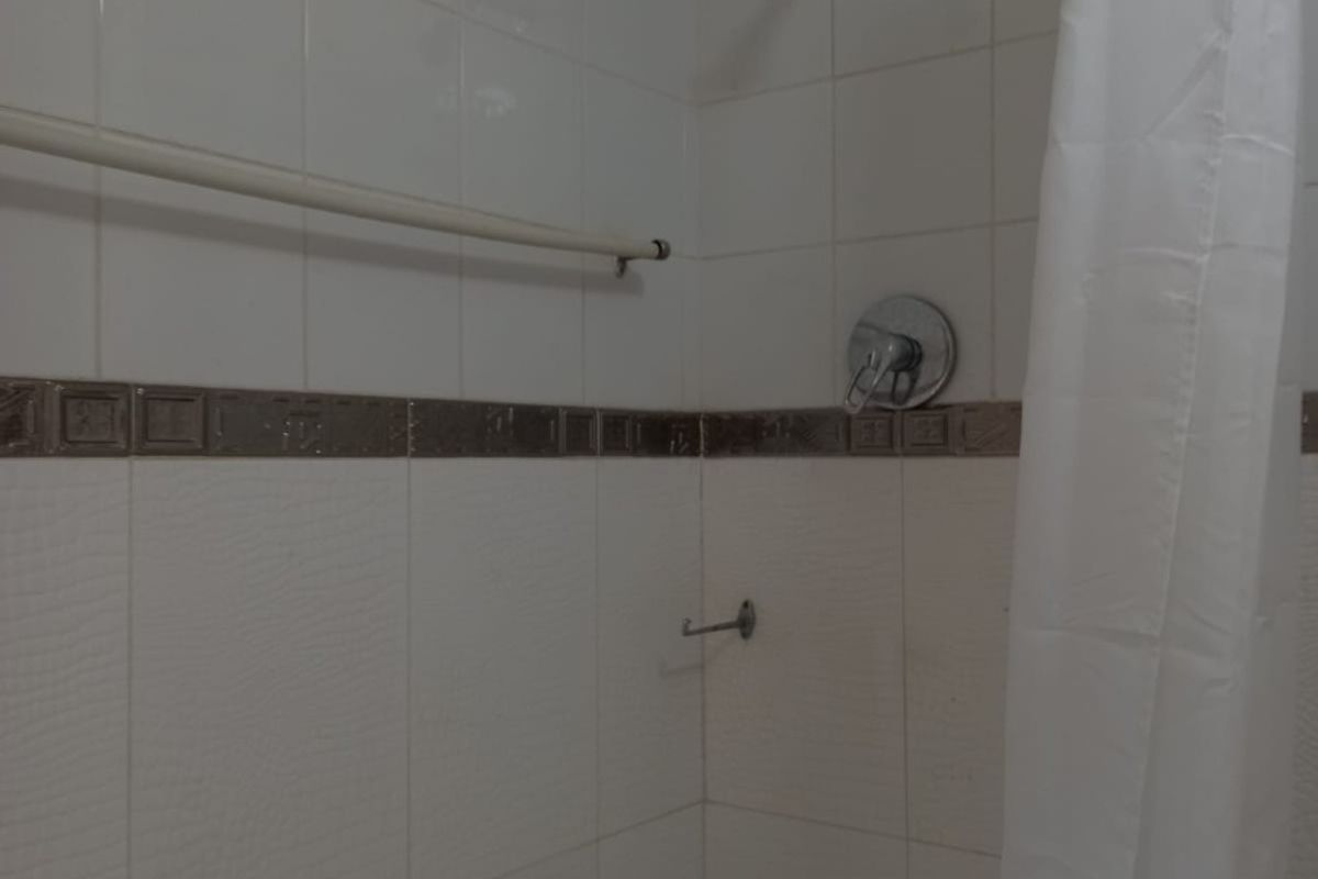 A functional bathroom shower area featuring white wall tiles with a decorative border, a standard shower mixer, and a wall-mounted towel rail.