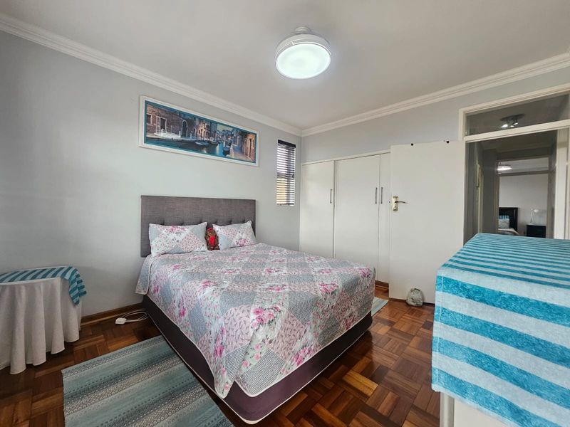 A well-maintained bedroom featuring classic parquet flooring, built-in cupboards, and decorative cornicing, offering a clean and functional living space.