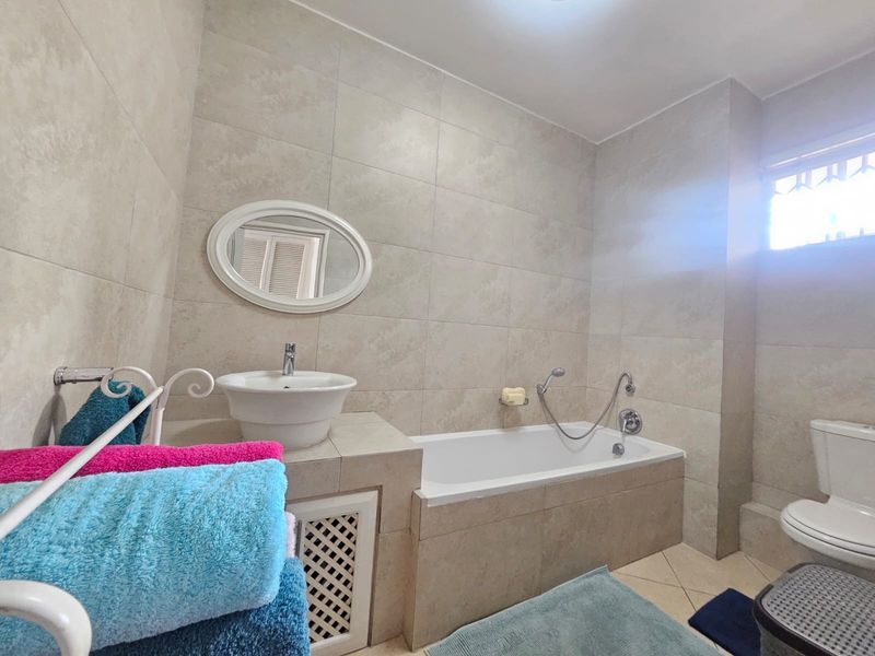 A well-maintained bathroom featuring neutral wall tiles, a built-in bathtub, a vessel sink, and a standard toilet.