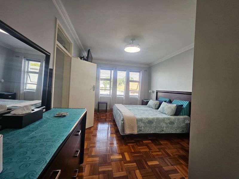 A well-maintained bedroom featuring classic parquet flooring, ceiling fan, and built-in storage, offering a comfortable and functional living space.