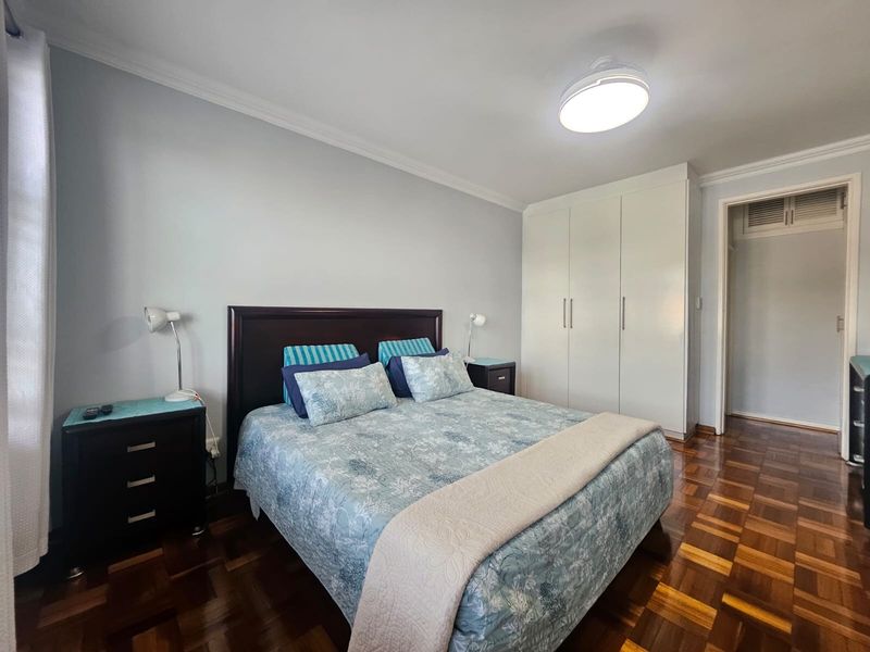 A well-maintained bedroom featuring classic parquet flooring, built-in wardrobes, and crown molding, providing a clean and functional living space.