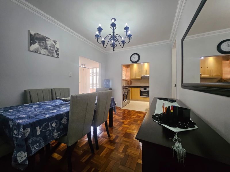 Open plan dining area featuring classic parquet flooring and crown molding, leading into a functional kitchen with built-in cabinetry and appliances.