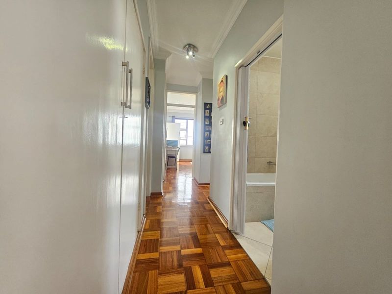 A bright hallway featuring polished parquet flooring, built-in storage cupboards, and access to adjacent rooms including a bathroom.