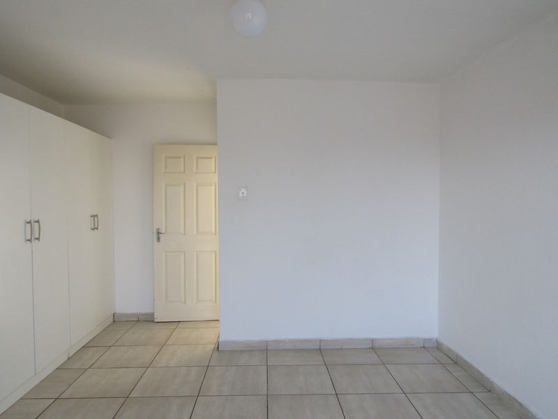 A clean, empty bedroom featuring neutral tiled flooring and built-in cupboards, providing a blank canvas for personalization.