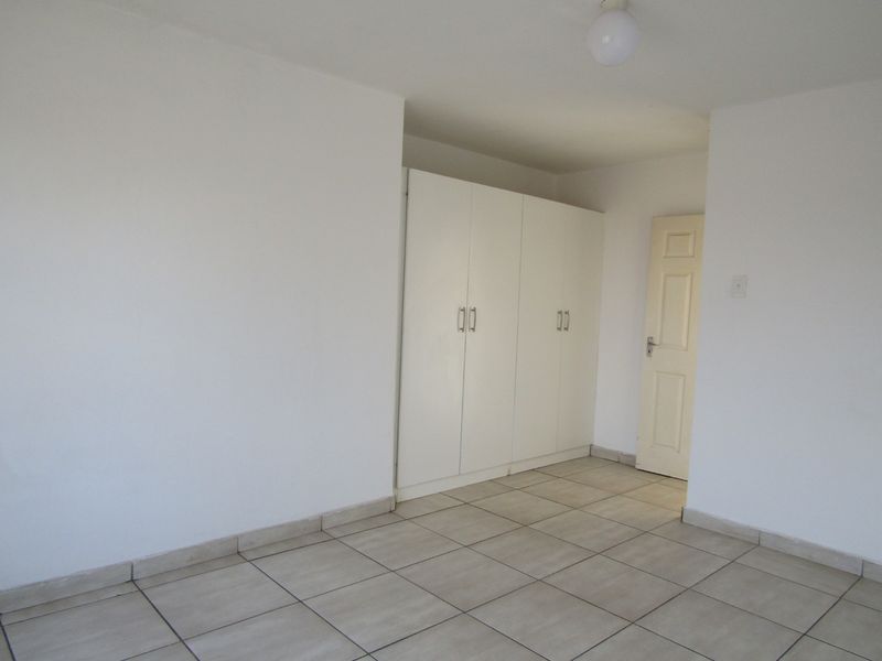 A clean, empty bedroom featuring neutral tiled flooring and built-in white cupboards, providing a blank canvas for personalization.