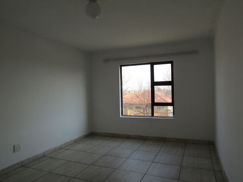 A vacant bedroom featuring neutral tiled flooring, white walls, and an aluminium-framed window with an installed curtain rail.