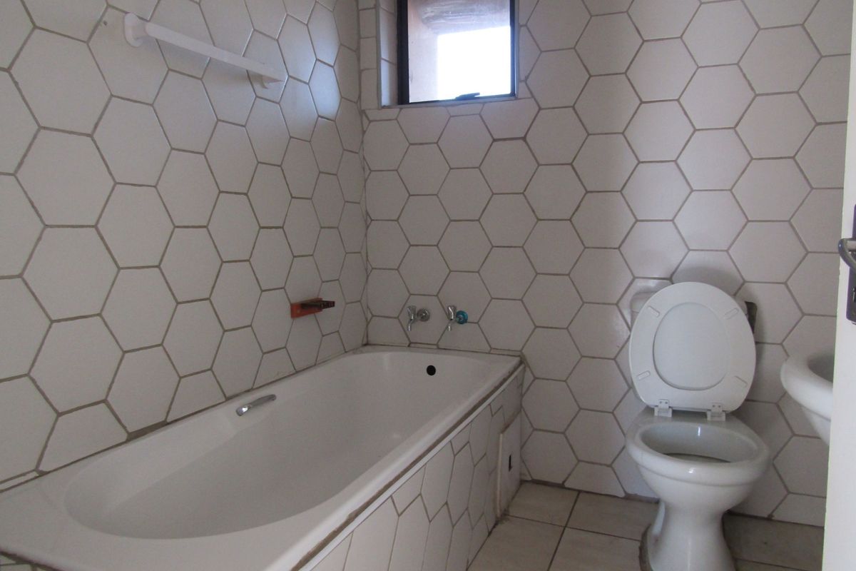 A functional bathroom featuring a bathtub, toilet, and basin with distinctive hexagonal wall tiling and a small window for natural light.
