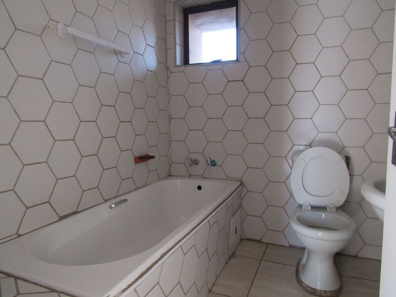 A functional bathroom featuring a bathtub, toilet, and basin with distinctive hexagonal wall tiling and a small window for natural light.