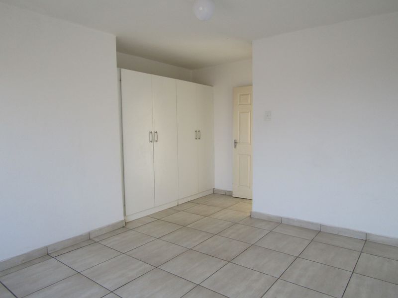An empty bedroom featuring neutral tiled flooring and white built-in cupboards, providing a clean and versatile space ready for personalization.