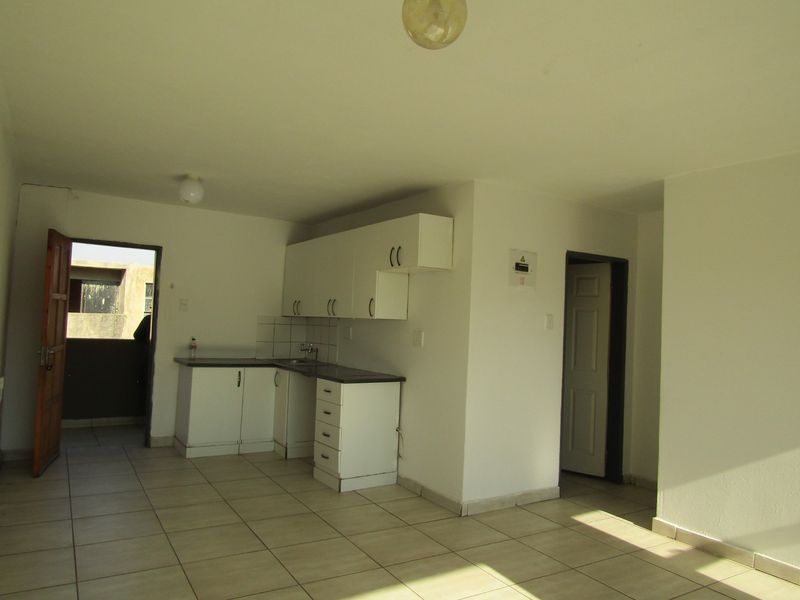 A compact, empty kitchen area featuring white built-in cabinetry, laminate countertops, and tiled flooring, providing a functional base for renovation.