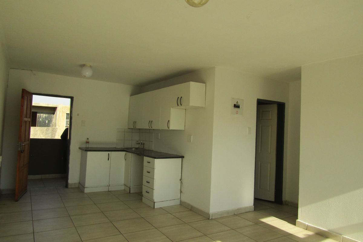 A compact, empty kitchen area featuring white built-in cabinetry, laminate countertops, and tiled flooring, providing a functional base for renovation.
