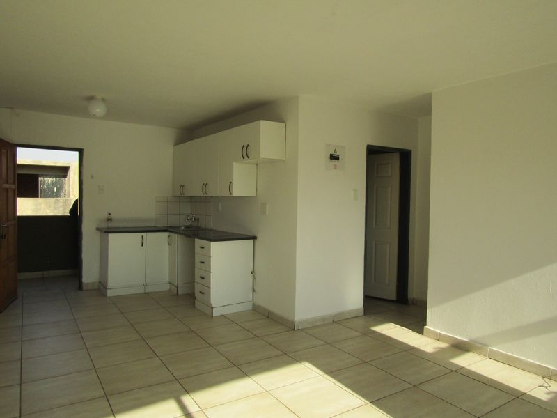 An open-plan living and kitchen area featuring tiled flooring, white cabinetry, and direct access to an outdoor space.