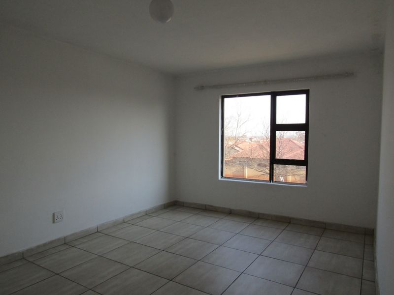 A bright, empty bedroom featuring neutral tiled flooring and a large aluminium-framed window, providing a blank canvas for personalization.