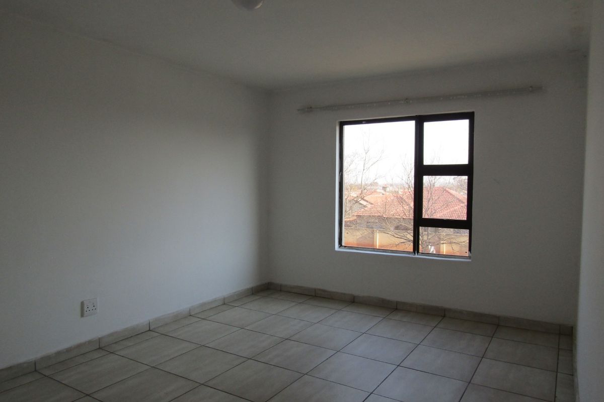 A bright, empty bedroom featuring neutral tiled flooring and a large aluminium-framed window, providing a blank canvas for personalization.