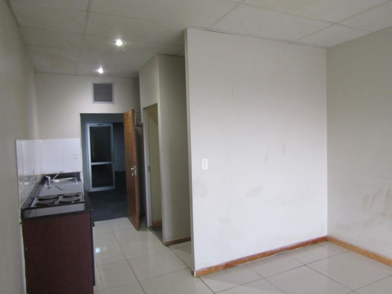 An empty open-plan living and kitchen area featuring tiled floors, a basic kitchenette with a built-in stove, and neutral wall finishes.