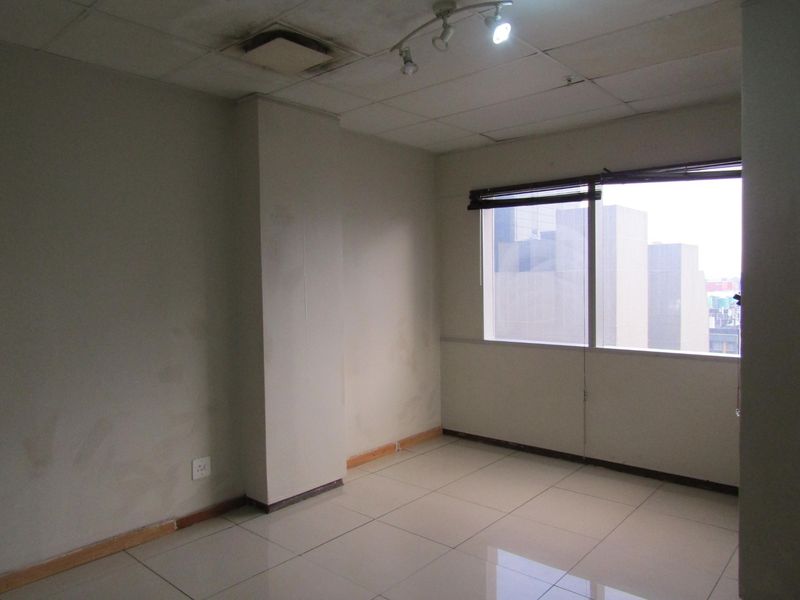 An empty bedroom featuring tiled flooring, a drop ceiling with track lighting, and a large window with city views.