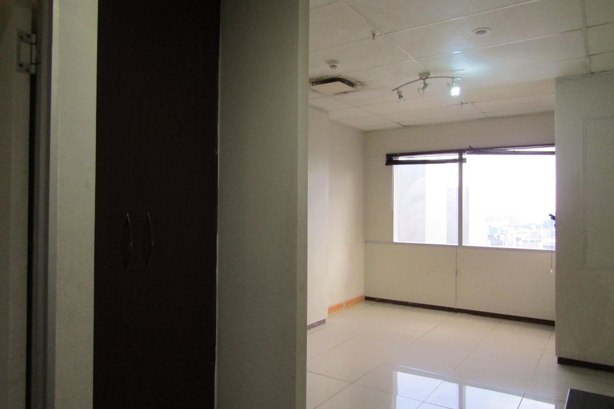 An empty living area featuring tiled flooring, a drop ceiling with track lighting, and a large window with city views.