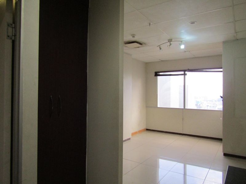 An empty living area featuring tiled flooring, a drop ceiling with track lighting, and a large window with city views.