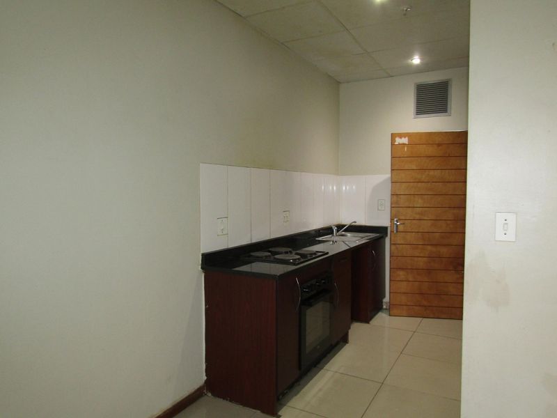 A compact, empty kitchen featuring dark wood cabinetry, black granite countertops, a built-in oven and hob, and tiled flooring.