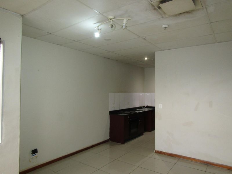 An empty open-plan living and kitchen area featuring tiled floors, a drop ceiling, and a compact kitchenette with built-in appliances.