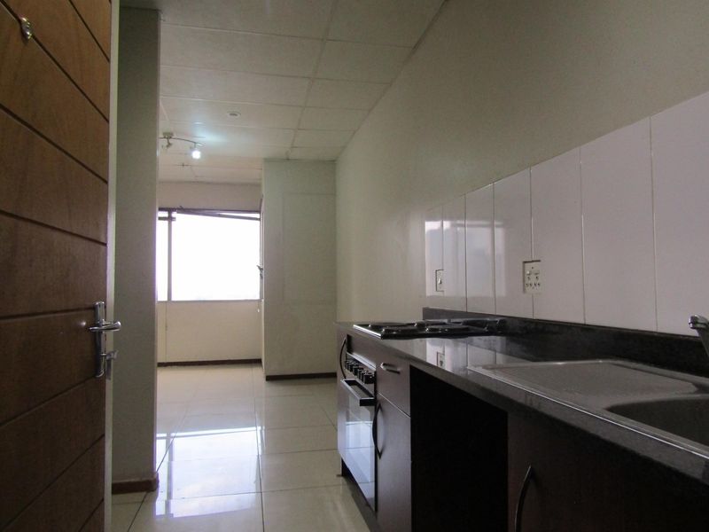 A functional kitchen area featuring built-in cabinetry, granite countertops, a built-in oven and hob, and tiled flooring, leading into an open living space.
