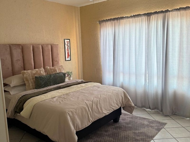 A bedroom featuring tiled flooring and a ceiling fan, with large windows allowing natural light into the space.