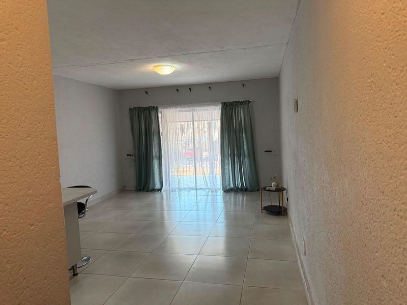 A spacious, neutrally finished living area featuring tiled flooring and a sliding glass door with security gate, providing access to the exterior.