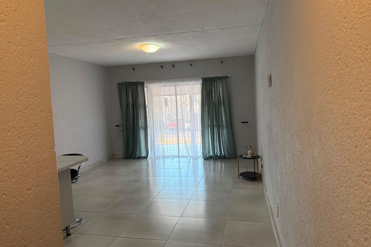 A spacious, neutrally finished living area featuring tiled flooring and a sliding glass door with security gate, providing access to the exterior.