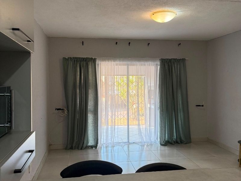 An open-plan living area featuring tiled floors, built-in cabinetry, and a sliding glass door with security gate leading to the exterior.