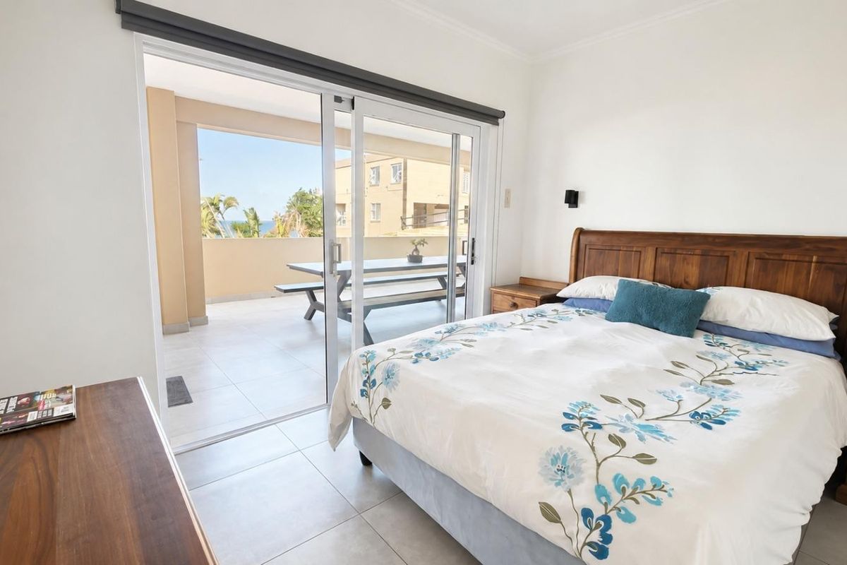 A bright bedroom featuring tiled flooring and large sliding glass doors that provide direct access to a private balcony with outdoor seating.