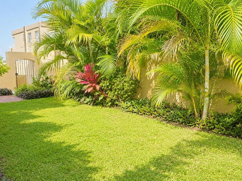 A well-maintained private garden featuring a lush lawn, mature palm trees, landscaped borders, and a secure gated entrance.