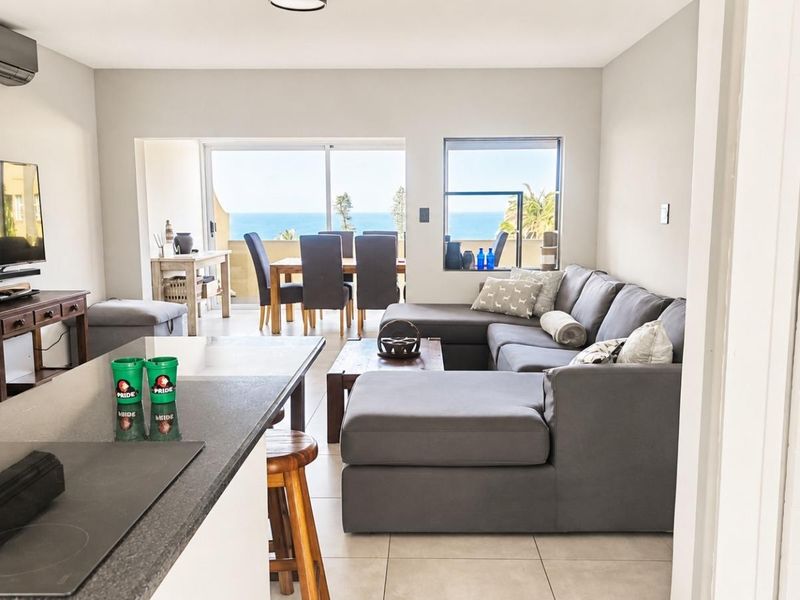 Spacious open-plan living and kitchen area featuring tiled floors, modern stone countertops, and large sliding doors opening to a scenic ocean view.