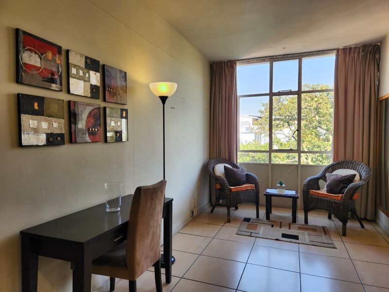 A bright living area featuring tiled flooring and a large window that provides natural light and a pleasant outdoor view.