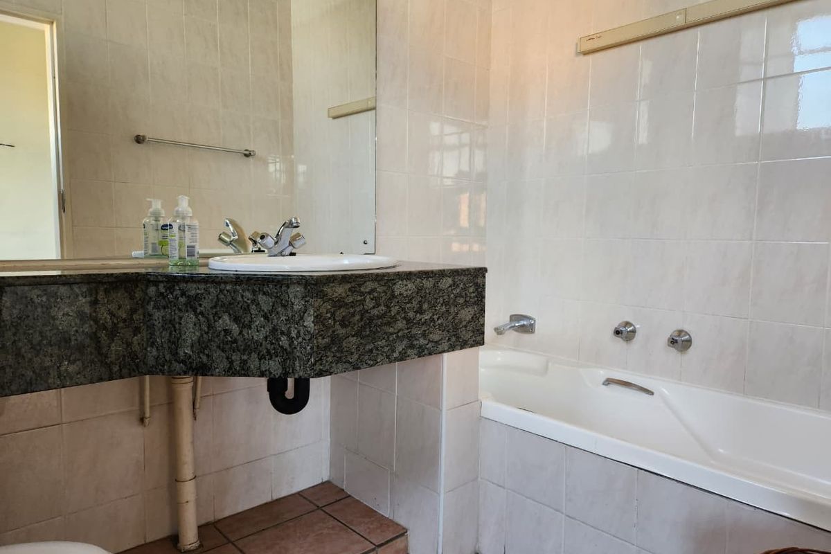 A functional bathroom featuring a granite vanity top, inset basin, and a built-in bathtub with wall-mounted chrome fixtures and neutral ceramic tiling.