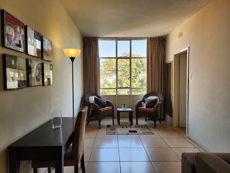 A living area featuring tiled flooring and a large window providing natural light, offering a functional space for relaxation or dining.