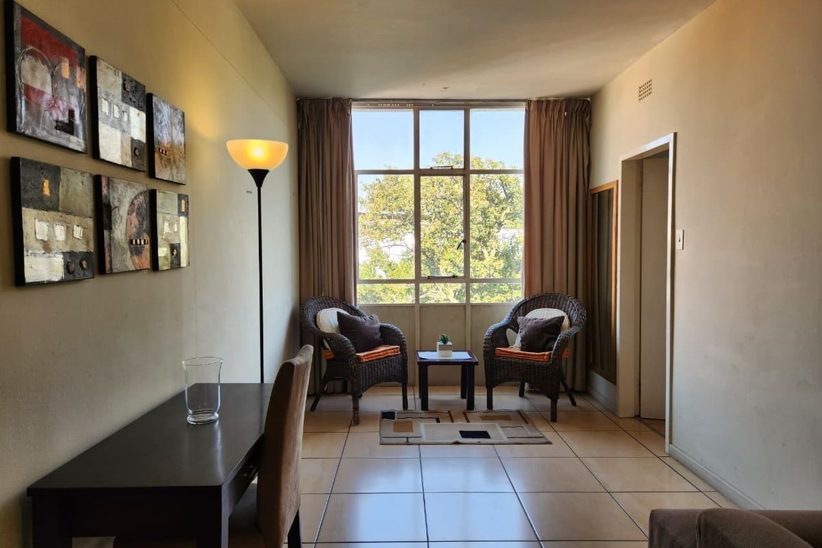 A living area featuring tiled flooring and a large window providing natural light, offering a functional space for relaxation or dining.