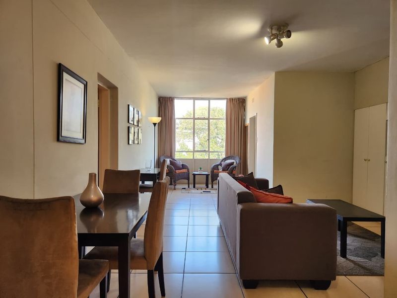 Open-plan living and dining area featuring tiled flooring, built-in storage, and a large window providing natural light.