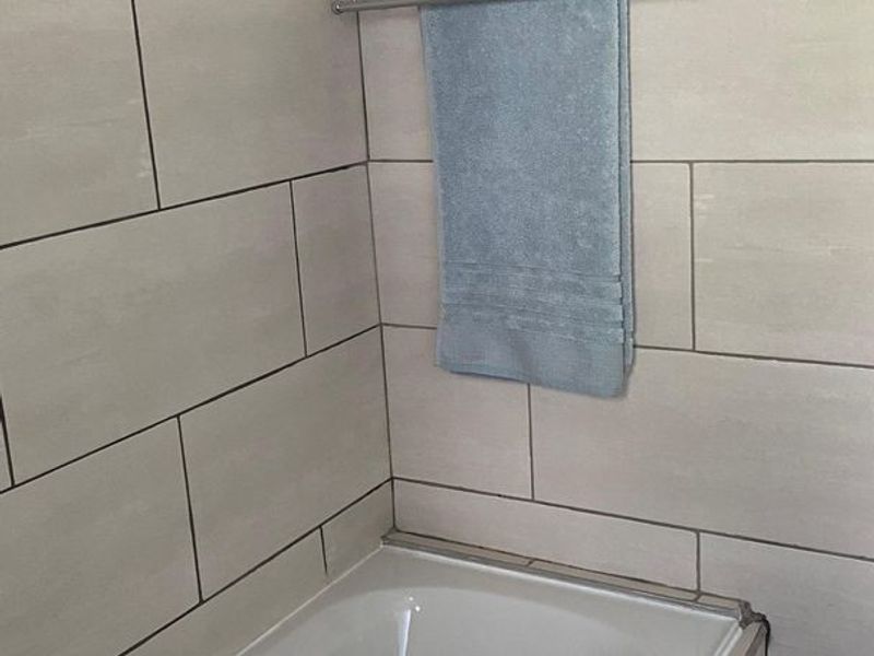 A bathroom featuring a standard bathtub with light-colored wall tiling and a chrome towel rail.