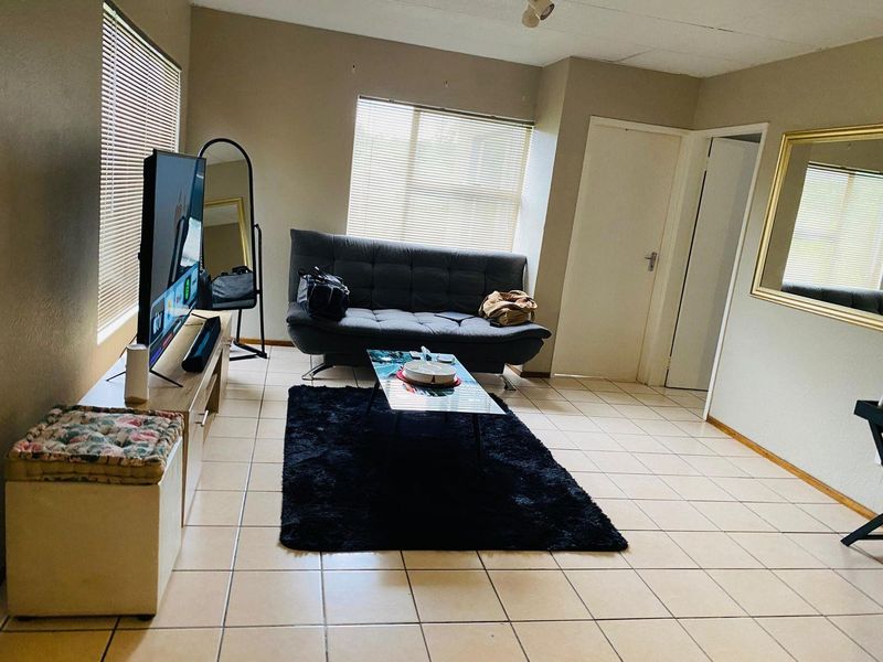 A living room featuring neutral tiled flooring and venetian blinds, offering a functional space with potential for cosmetic updates.