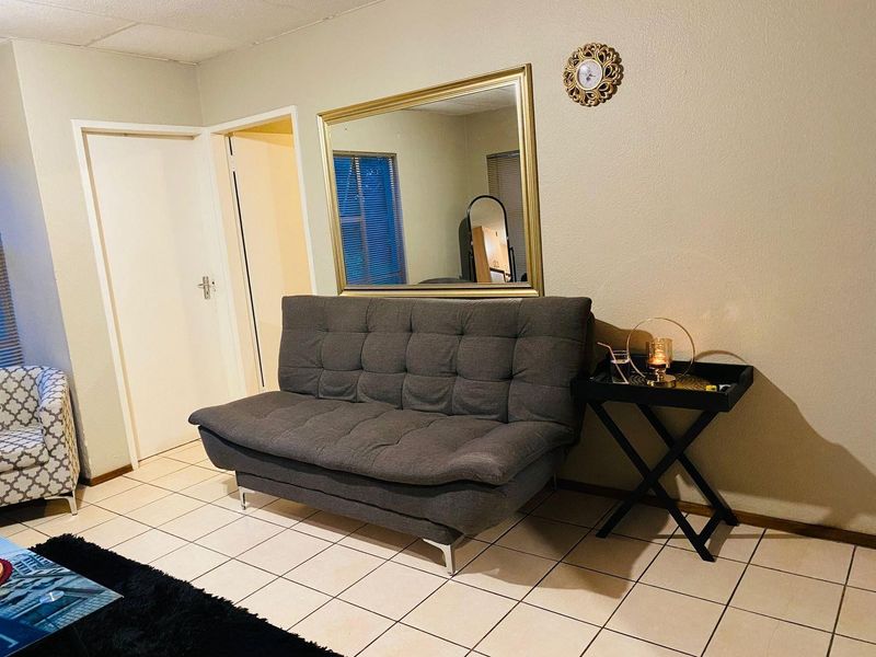 A living area featuring neutral wall finishes and tiled flooring, providing a functional space with access to adjacent rooms.