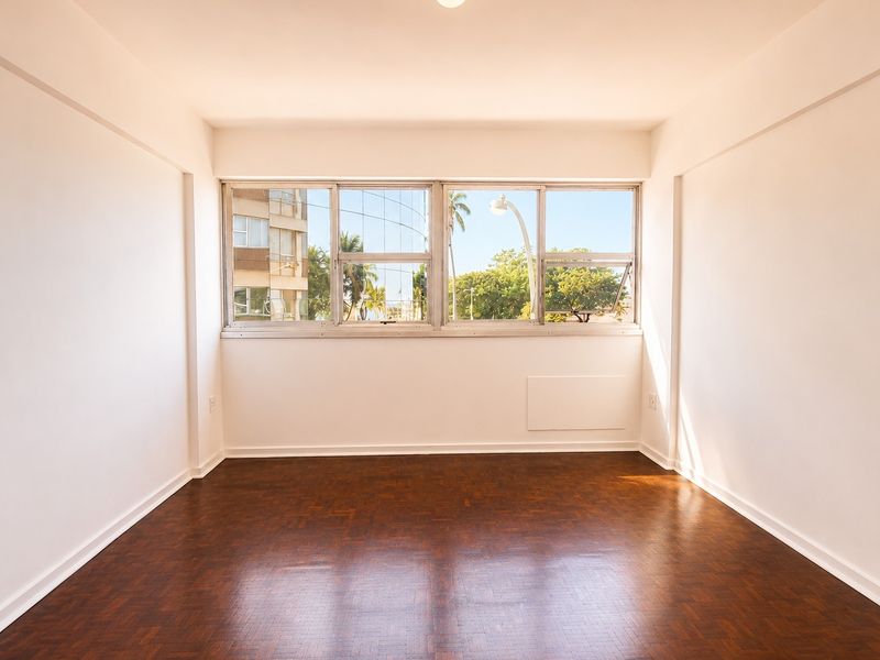 A bright, empty bedroom featuring polished parquet flooring and large windows with natural light, offering a clean canvas for interior design.