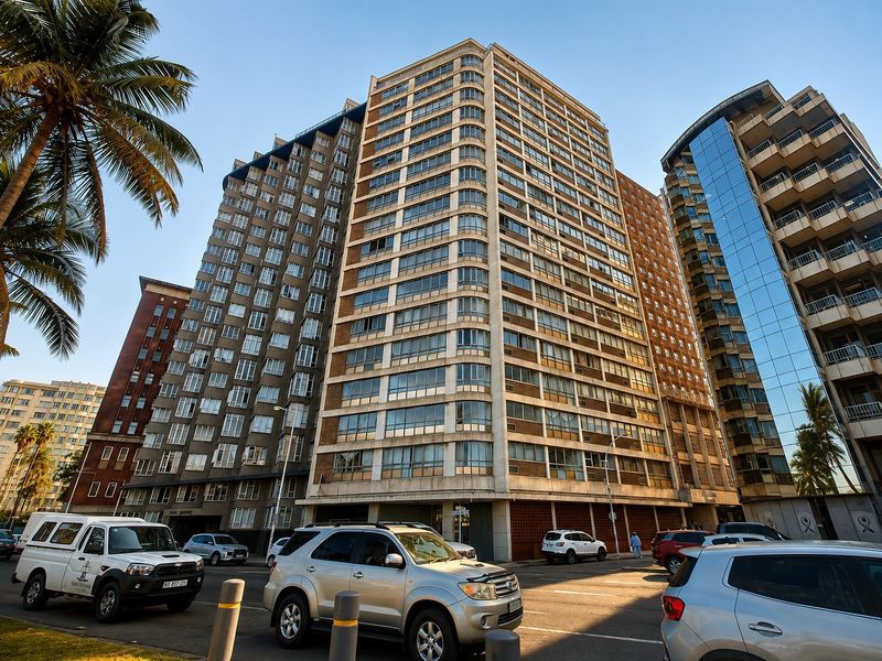 A street-level view of a multi-story apartment building facade featuring large windows and a concrete exterior structure in an urban setting.